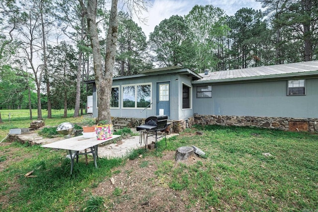 back of house featuring metal roof, a lawn, and view of scattered trees