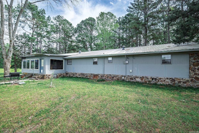 back of house with metal roof, a lawn, and view of scattered trees