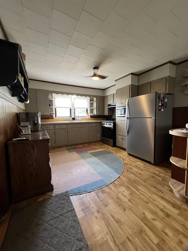kitchen with appliances with stainless steel finishes, gray cabinets, a sink, dark countertops, and light wood-style flooring