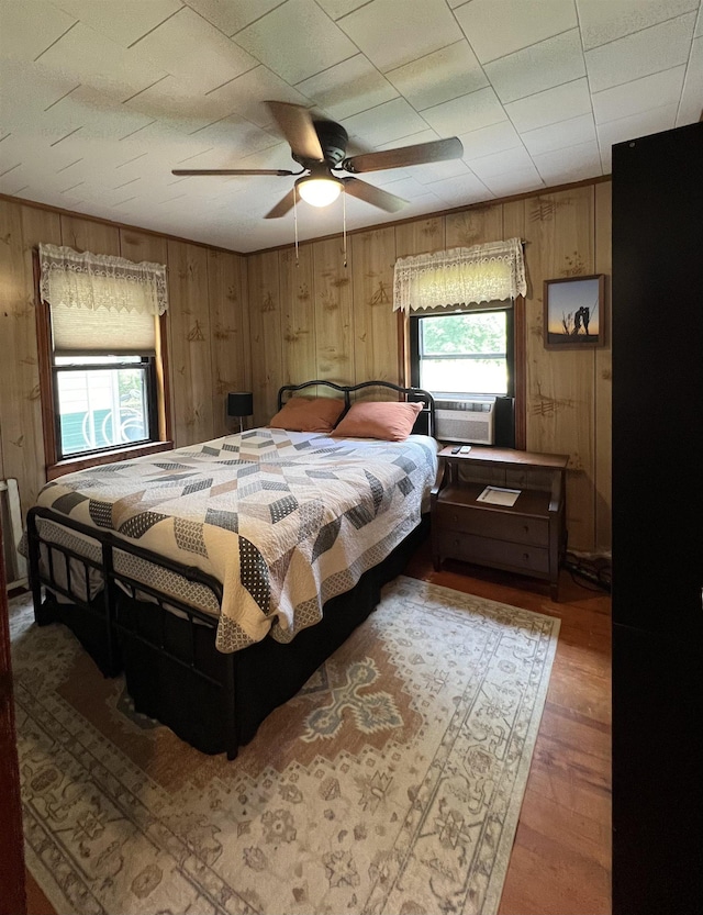 bedroom featuring cooling unit, wood walls, wood finished floors, and ceiling fan