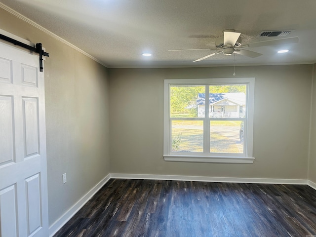 empty room featuring a barn door, ornamental molding, dark wood-style floors, baseboards, and ceiling fan