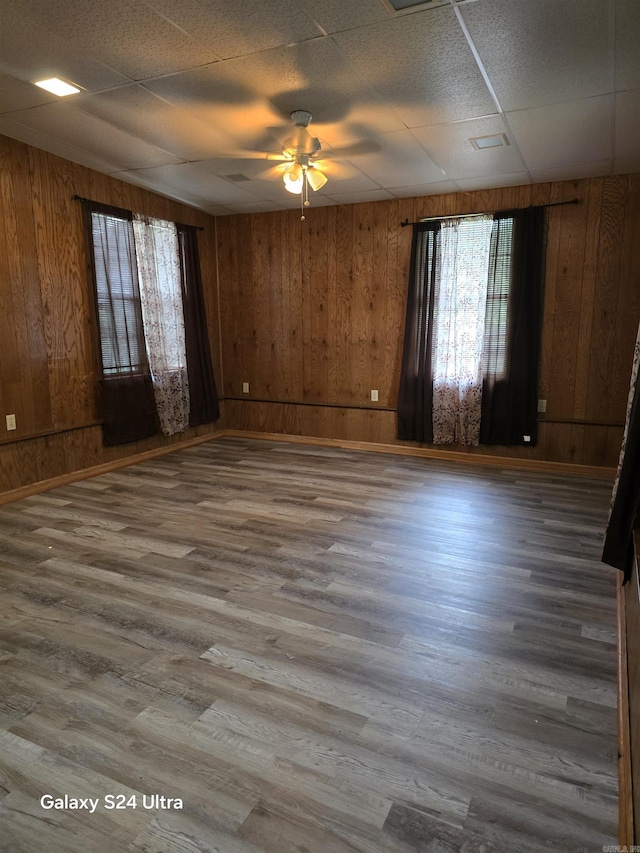 spare room featuring a ceiling fan, wood walls, wood finished floors, and baseboards