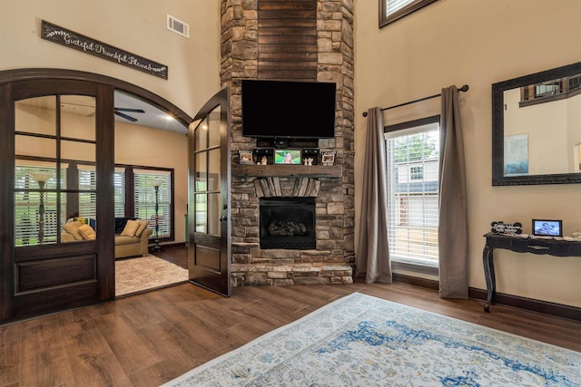 living room featuring dark wood finished floors, a fireplace, a towering ceiling, baseboards, and a ceiling fan