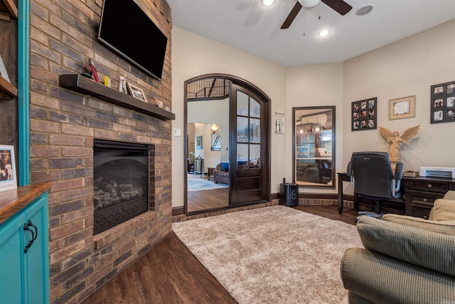 living room featuring a ceiling fan, dark wood-style floors, a fireplace, arched walkways, and an office area