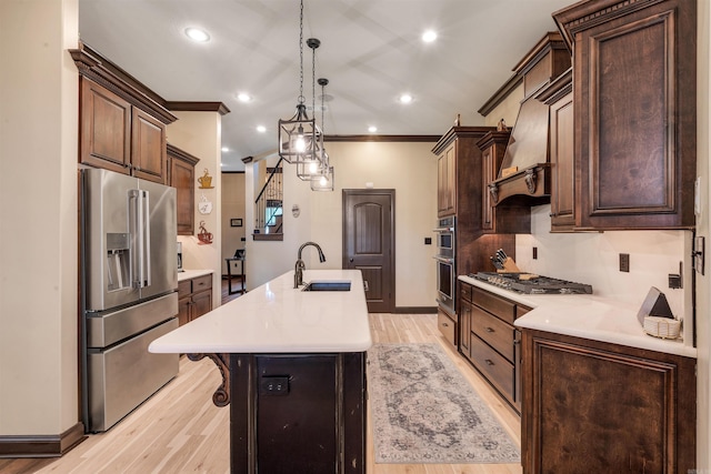 kitchen with appliances with stainless steel finishes, a sink, an island with sink, light countertops, and light wood-style floors