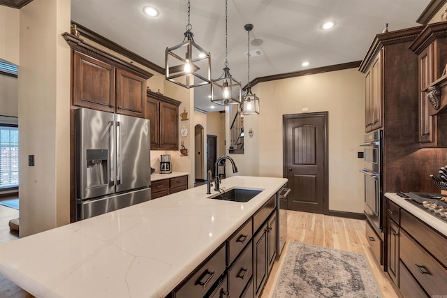 kitchen featuring appliances with stainless steel finishes, a sink, a kitchen island with sink, ornamental molding, and light wood-style floors
