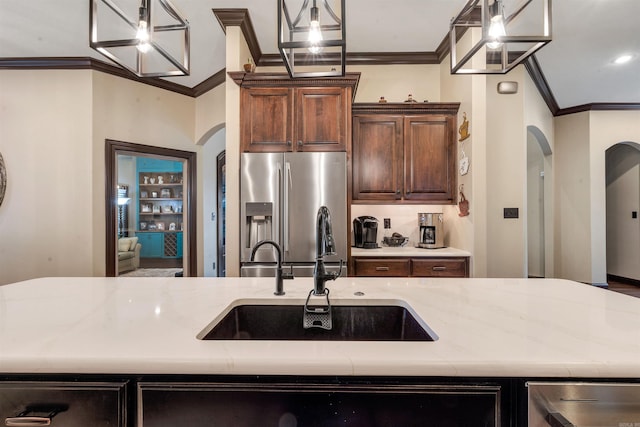 kitchen featuring arched walkways, appliances with stainless steel finishes, a sink, crown molding, and a kitchen island with sink