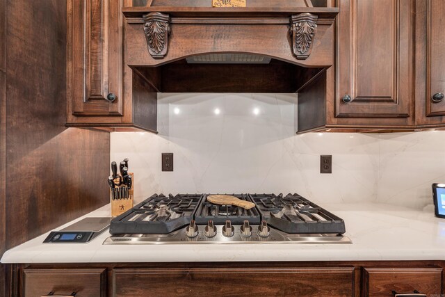 kitchen featuring stainless steel gas stovetop, premium range hood, tasteful backsplash, light countertops, and dark brown cabinets