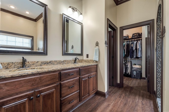 full bath featuring crown molding, wood finished floors, baseboards, double vanity, and a spacious closet