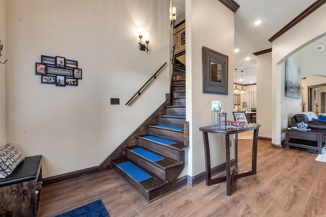 stairway featuring baseboards, wood finished floors, recessed lighting, crown molding, and a chandelier