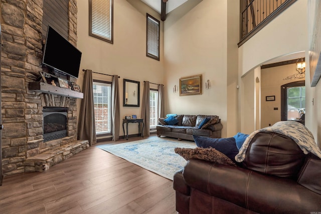 living area featuring arched walkways, a stone fireplace, healthy amount of natural light, a towering ceiling, and wood finished floors