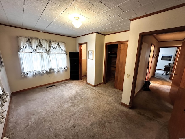 unfurnished bedroom with crown molding, carpet flooring, baseboards, and a closet