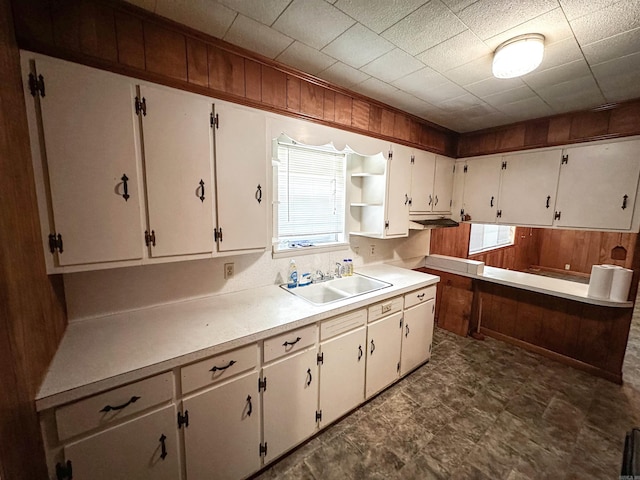 kitchen featuring a sink, wooden walls, open shelves, white cabinets, and light countertops