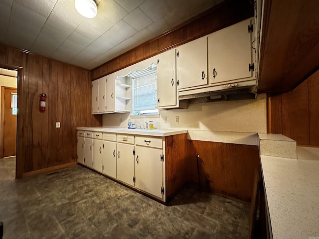 kitchen with wooden walls, white cabinetry, light countertops, under cabinet range hood, and dark flooring