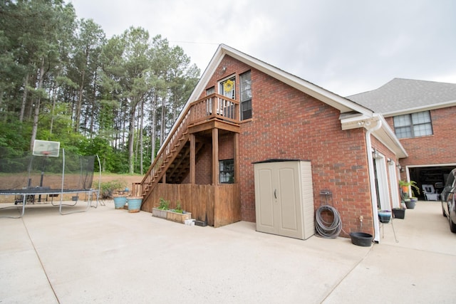 back of property featuring a trampoline, brick siding, stairway, and a patio