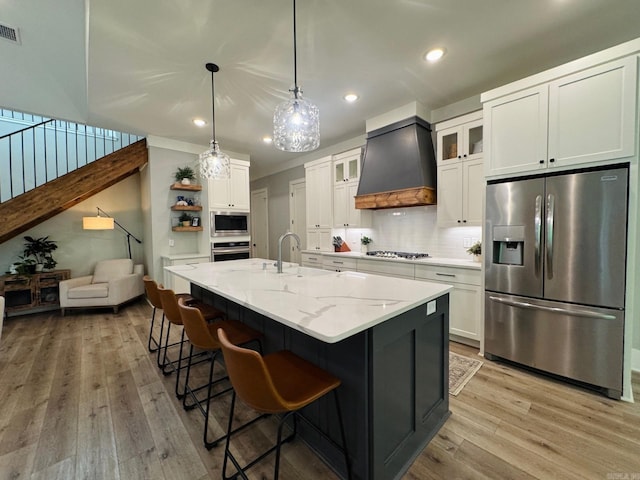 816 Nature Way, Benton, AR 72019 - kitchen featuring stainless steel appliances, premium range hood, light wood-style floors, tasteful backsplash, and white cabinetry