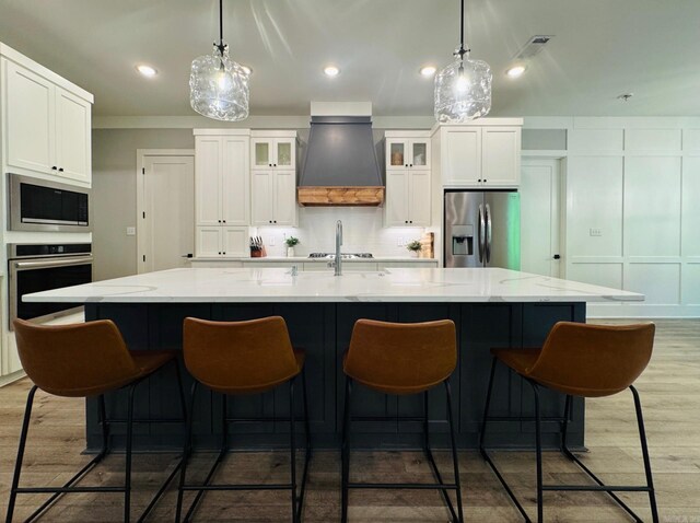 816 Nature Way, Benton, AR 72019 - kitchen with stainless steel appliances, premium range hood, white cabinets, wood finished floors, and a kitchen bar