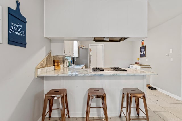 kitchen with a peninsula, appliances with stainless steel finishes, white cabinetry, a breakfast bar, and a sink