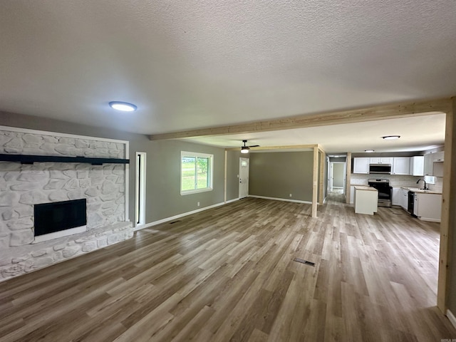 27 Grant 491 Rd, Sheridan, AR 72105 - unfurnished living room with a stone fireplace, wood finished floors, beam ceiling, baseboards, and ceiling fan