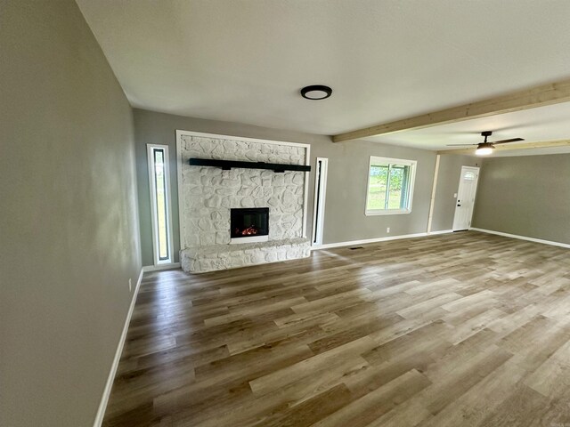 27 Grant 491 Rd, Sheridan, AR 72105 - unfurnished living room featuring baseboards, a stone fireplace, wood finished floors, beamed ceiling, and a ceiling fan