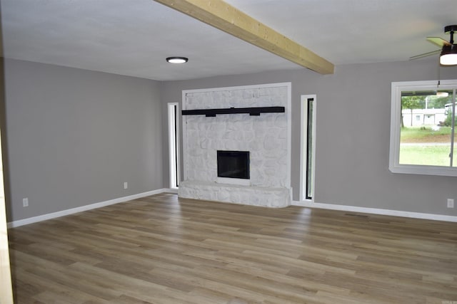 27 Grant 491 Rd, Sheridan, AR 72105 - unfurnished living room with beamed ceiling, baseboards, wood finished floors, a stone fireplace, and a ceiling fan