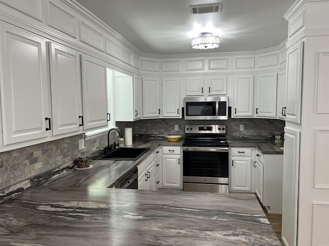 1906 Fernwood Cv, Benton, AR 72015 - kitchen featuring appliances with stainless steel finishes, dark countertops, white cabinets, a sink, and decorative backsplash