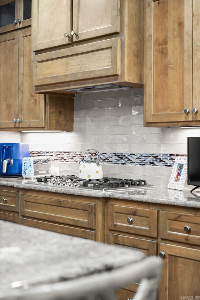 216 Lake Valley Dr, Maumelle, AR 72113 - kitchen with backsplash, light stone counters, brown cabinets, glass insert cabinets, and stainless steel gas stovetop