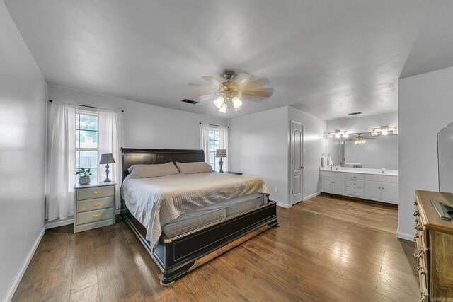 bedroom featuring multiple windows, dark wood-type flooring, baseboards, and connected bathroom