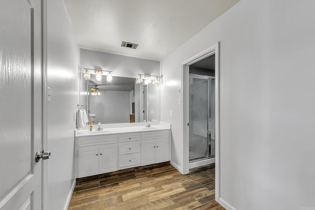 full bath featuring wood finished floors, a stall shower, double vanity, a ceiling fan, and baseboards