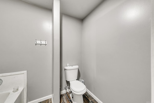 bathroom featuring toilet, a tub to relax in, wood finished floors, and baseboards