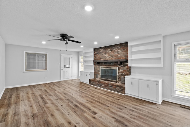 718 Coulter Rd, Sherwood, AR 72120 - unfurnished living room with a textured ceiling, baseboards, light wood finished floors, ceiling fan, and a fireplace