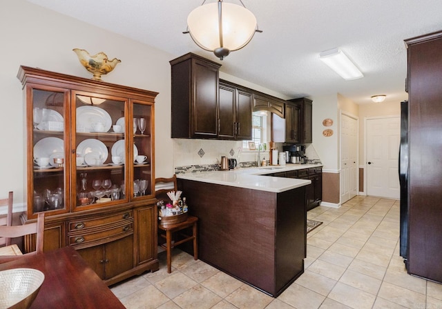kitchen featuring light countertops, dark brown cabinets, a peninsula, a sink, and light tile patterned flooring