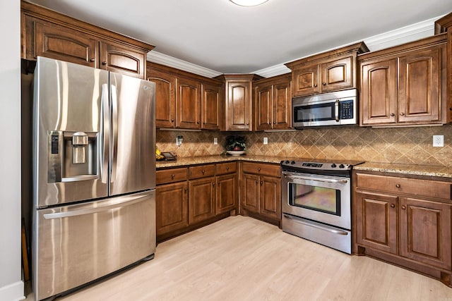 kitchen with stainless steel appliances, light stone counters, light wood finished floors, and tasteful backsplash