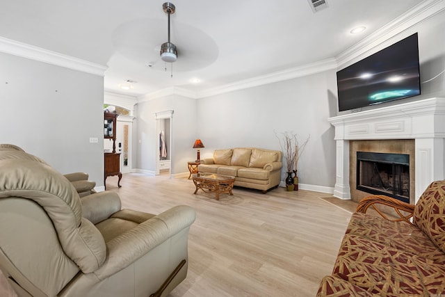 living room featuring a ceiling fan, baseboards, light wood-style floors, crown molding, and a tiled fireplace