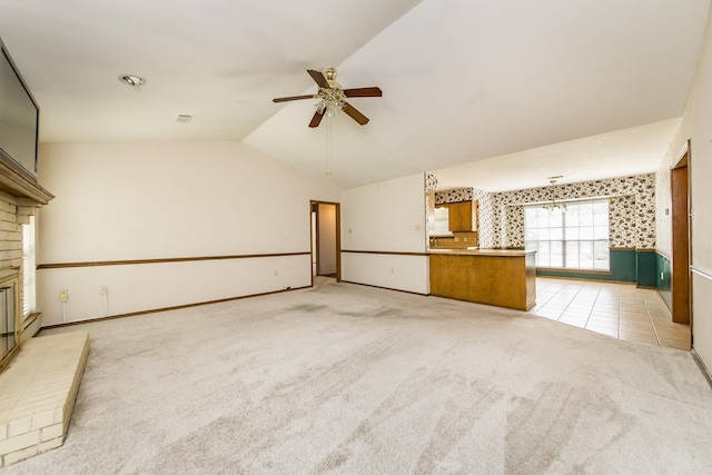 unfurnished living room featuring ceiling fan, vaulted ceiling, light colored carpet, a fireplace, and baseboards