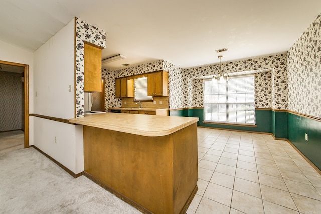 kitchen with wallpapered walls, a wainscoted wall, a sink, brown cabinets, and baseboards