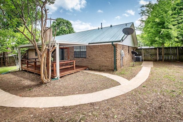 rear view of property featuring fence, brick siding, a deck, metal roof, and central air condition unit