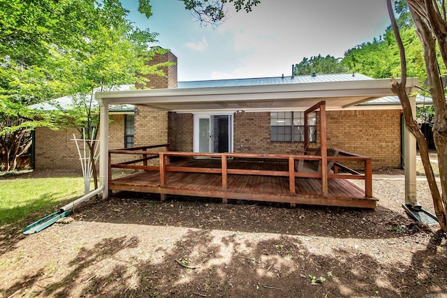 rear view of property featuring brick siding, a chimney, a wooden deck, and metal roof