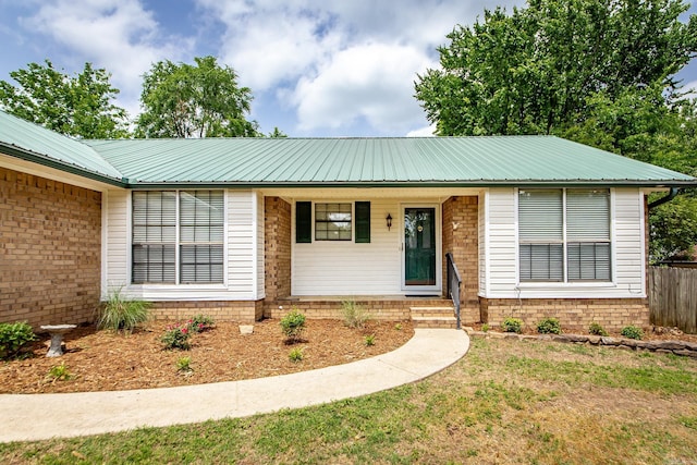 ranch-style house featuring metal roof, covered porch, and fence