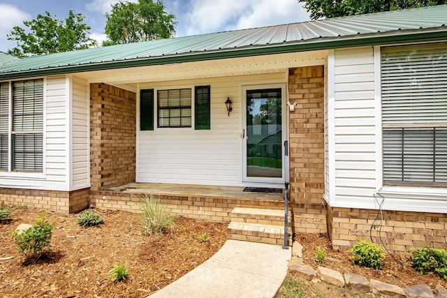 view of exterior entry featuring covered porch, metal roof, and brick siding