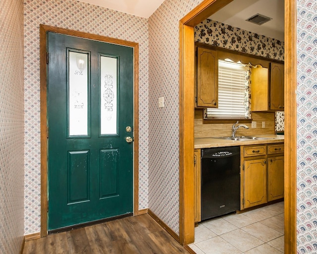 kitchen with black dishwasher, a sink, wallpapered walls, light countertops, and baseboards
