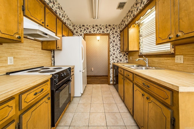 kitchen featuring black appliances, under cabinet range hood, a sink, light tile patterned floors, and brown cabinets