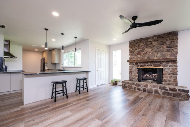 1117 Wild Turkey Ct, Little Rock, AR 72211 - kitchen featuring wall chimney range hood, light wood-type flooring, dark countertops, ceiling fan, and a kitchen breakfast bar