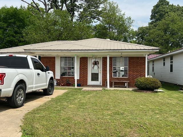 view of front of property with brick siding, a front lawn, and metal roof