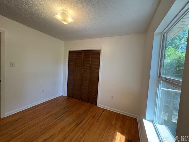 4900 Lochridge Rd, North Little Rock, AR 72116 - unfurnished bedroom featuring wood finished floors, a closet, a textured ceiling, and baseboards