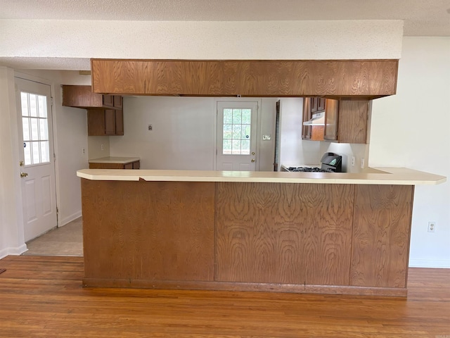 4900 Lochridge Rd, North Little Rock, AR 72116 - kitchen featuring under cabinet range hood, a peninsula, range with gas stovetop, and light wood-style flooring