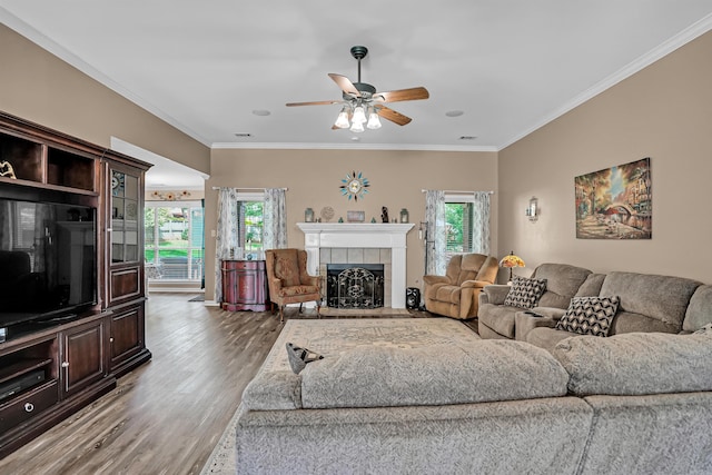 living area featuring a ceiling fan, wood finished floors, ornamental molding, and a tiled fireplace