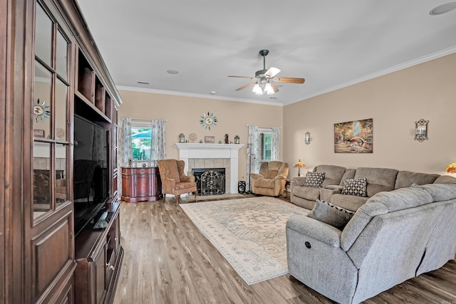 living room with wood finished floors, a ceiling fan, ornamental molding, and a fireplace