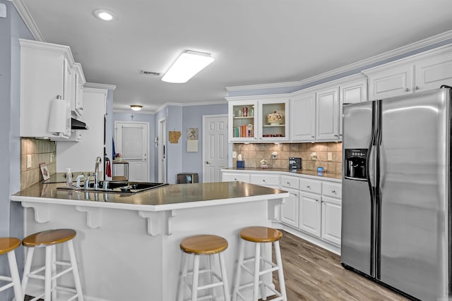 kitchen featuring stainless steel fridge with ice dispenser, a peninsula, a kitchen bar, white cabinetry, and decorative backsplash