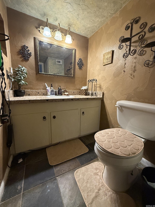 bathroom featuring toilet, a textured ceiling, vanity, and a textured wall